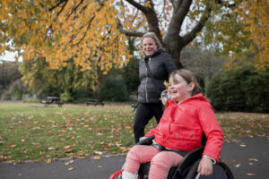 a girl using a wheelchair and her mother enjoy an outing to a park during autumn