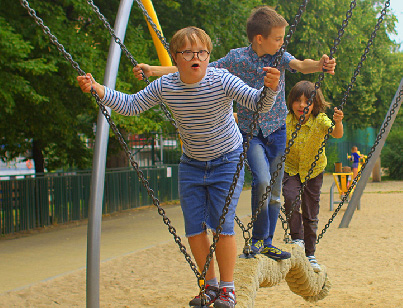 A group of school aged children ride a standing swing together in a park.
