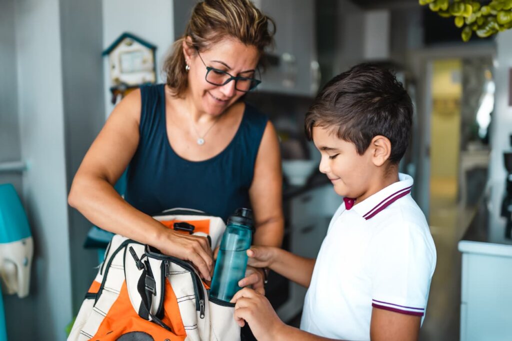 A single Mum helps her primary school-aged son pack his bag for school.