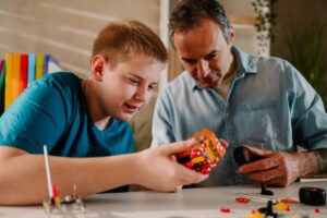 A teenage boy and his dad are at home building a model car. They work together in the study.