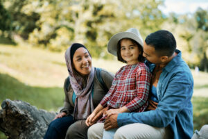 Muslim family, two parents and one daughter enjoying in spring day in nature. Focus is on little girl with straw hat looking at camera.