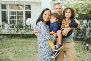 A mother and father hold their two young sons, posing for a picture on the grass at their house.